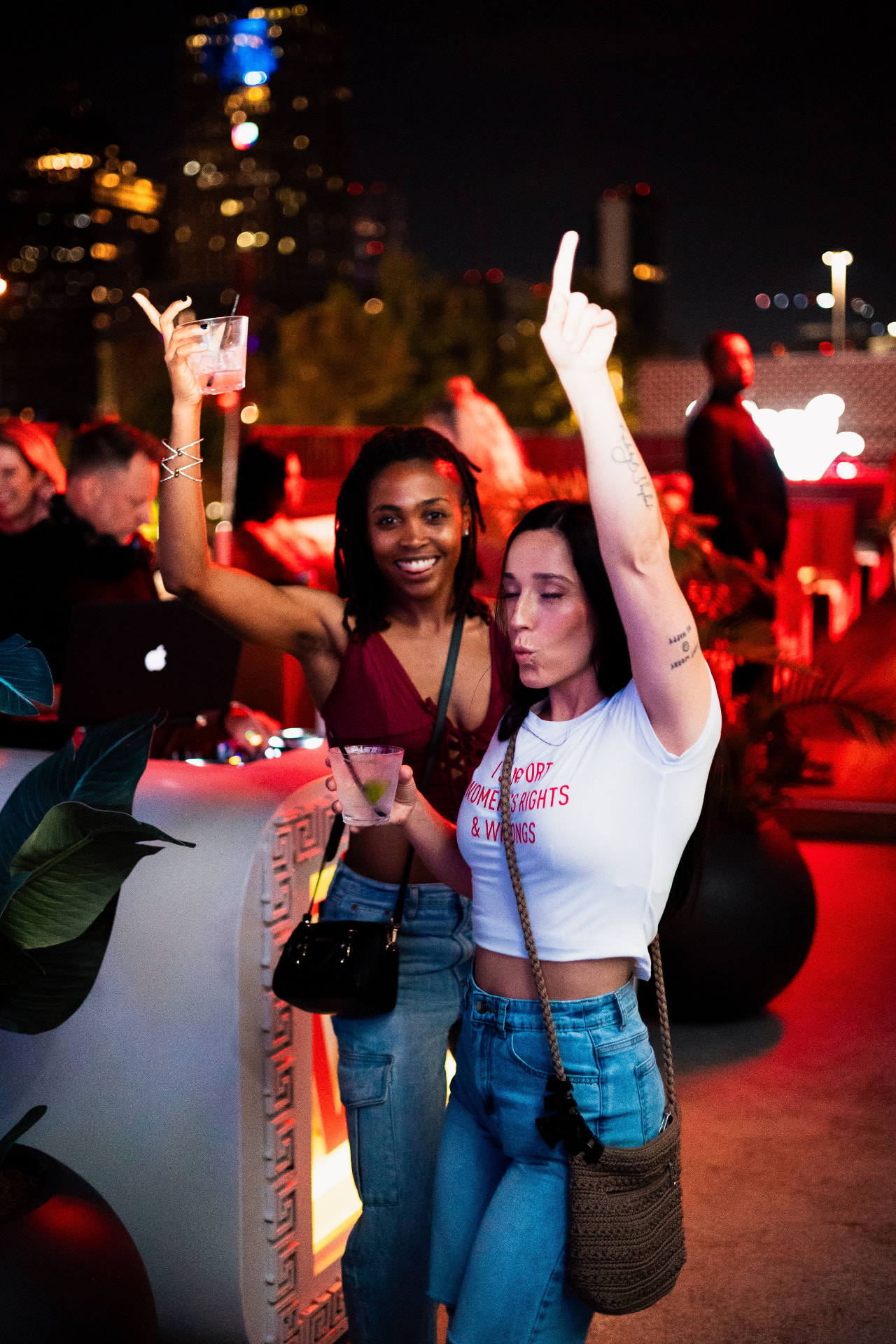 Two friends dancing with cocktails raised on the Vice Park rooftop with the Dallas skyline behind them